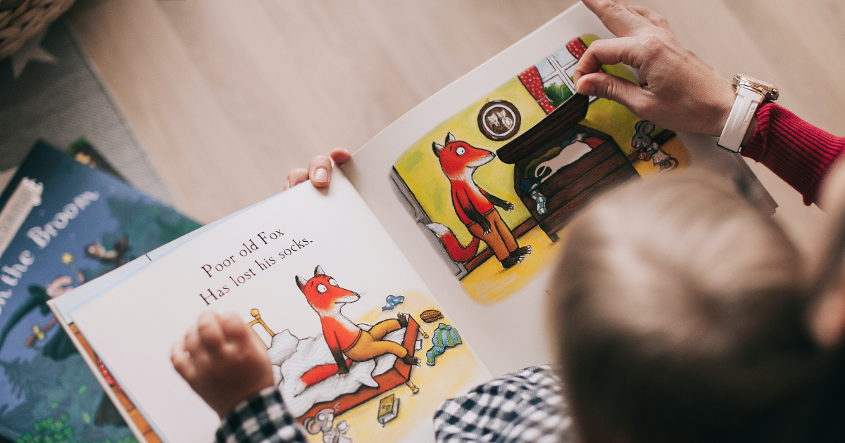 Child being read a book by an older person while sat on their lap.